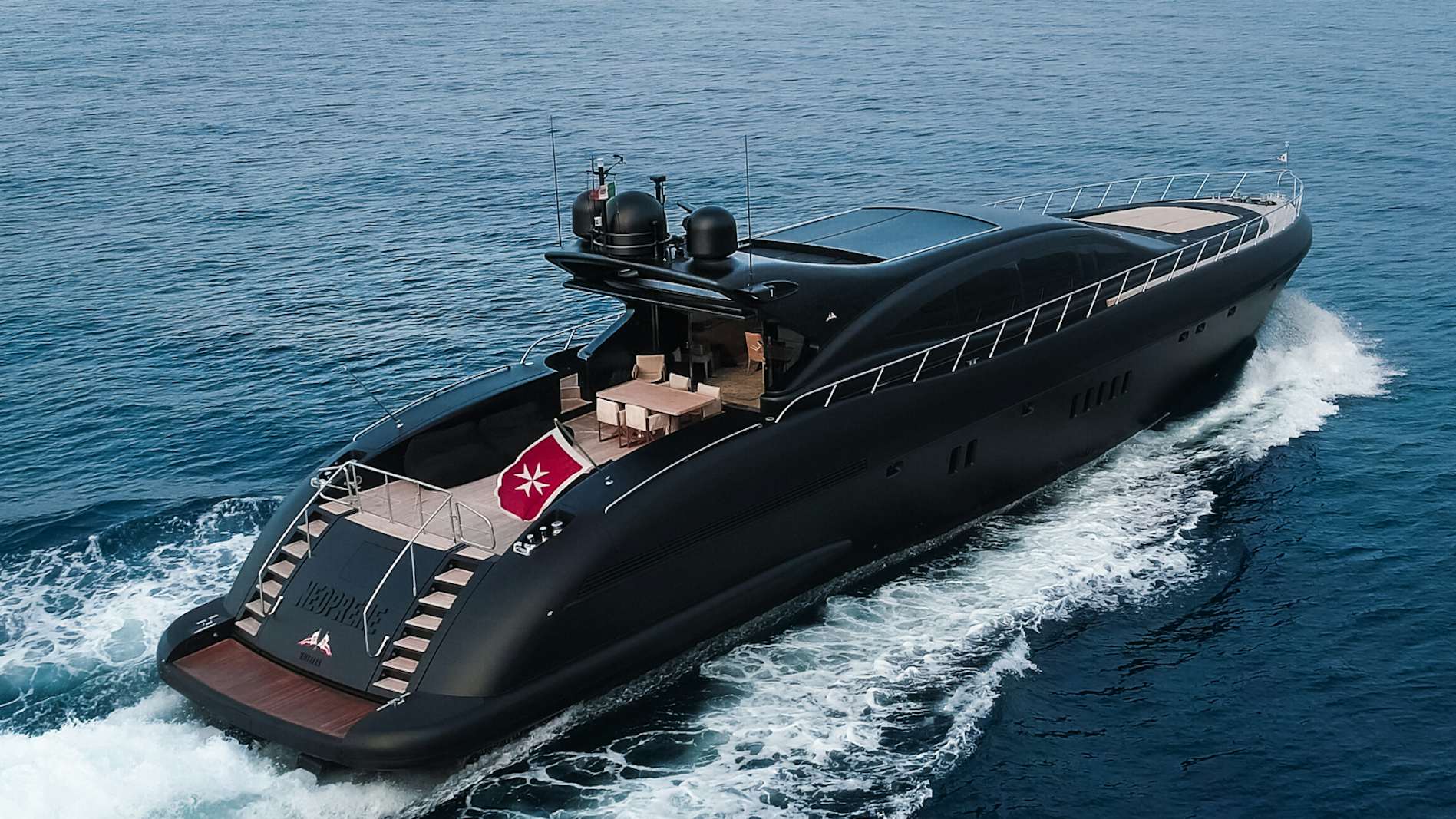 A sleek black Mangusta 108 yacht cruising on the ocean, its deck featuring an outdoor lounge and dining area.