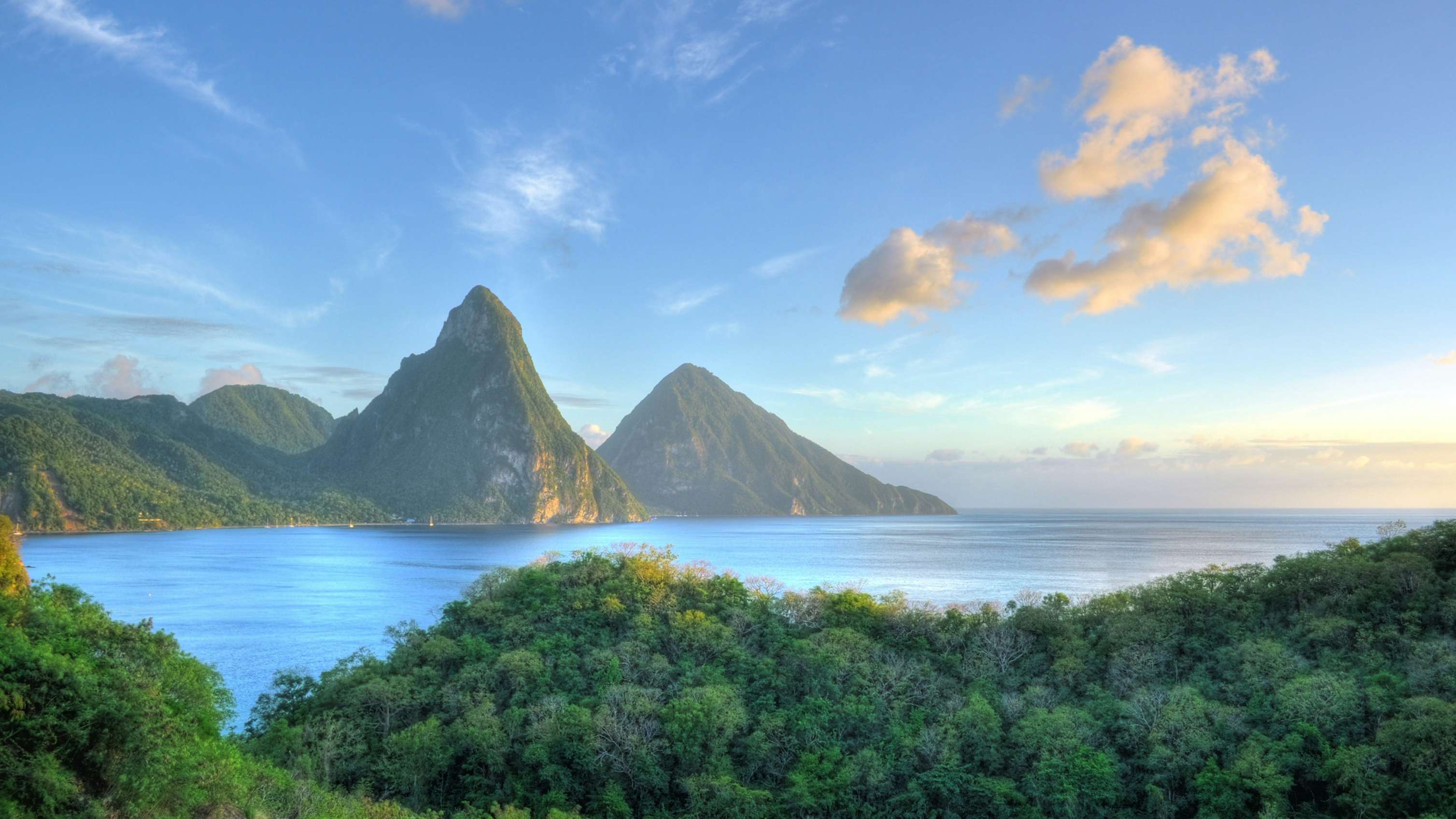 A serene daytime view of St. Lucia, featuring white sand beaches, untouched green nature, and foggy, high, pointed mountains in the background—a captivating scene for your Caribbean St. Lucia Charter Yacht journey.