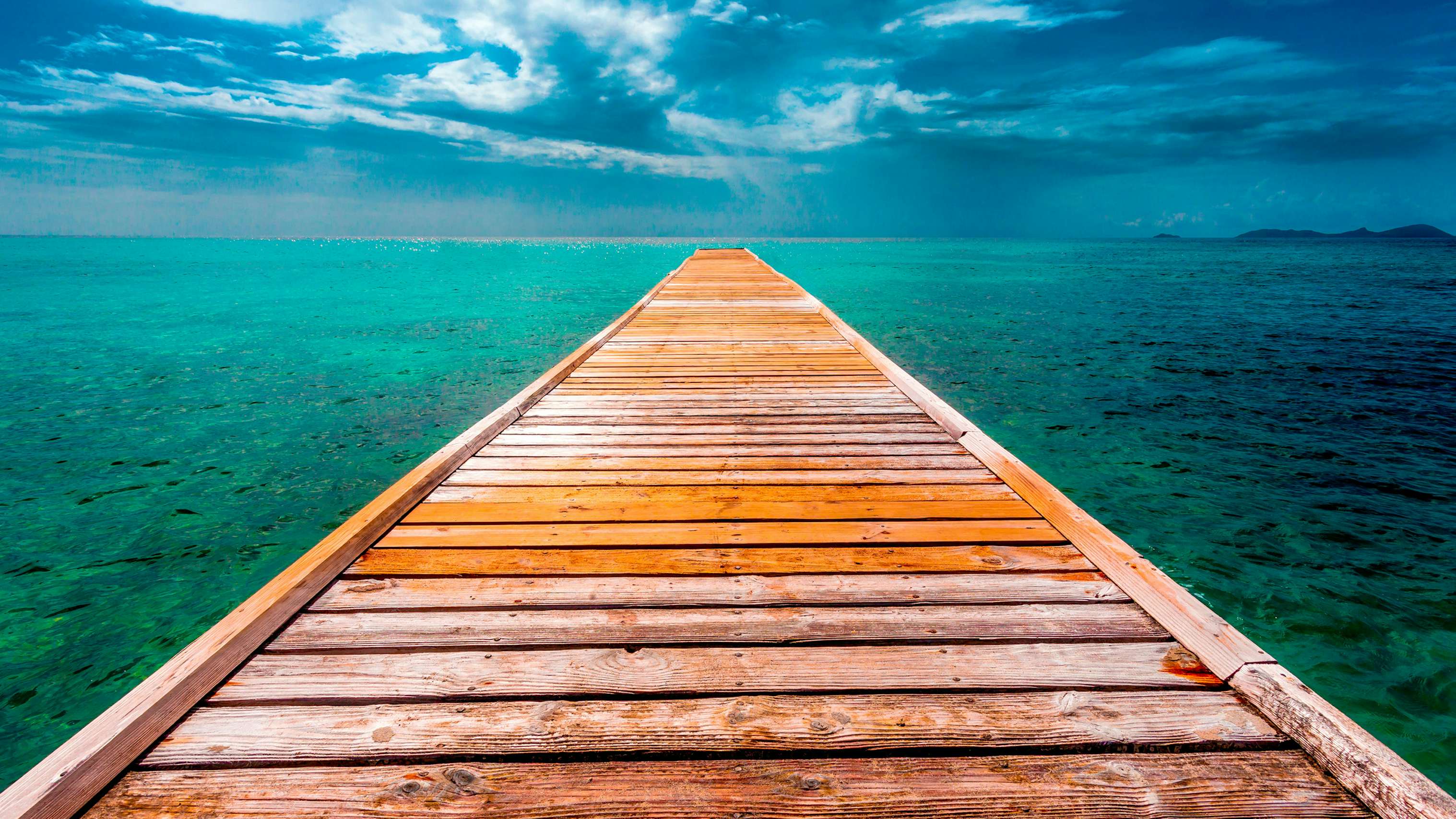 A vision of elegance in Mustique, St. Vincent and the Grenadines—a long wooden dock extending into super clear and vivid blue waters, inviting luxury on a Grenadines Superyacht Charter.