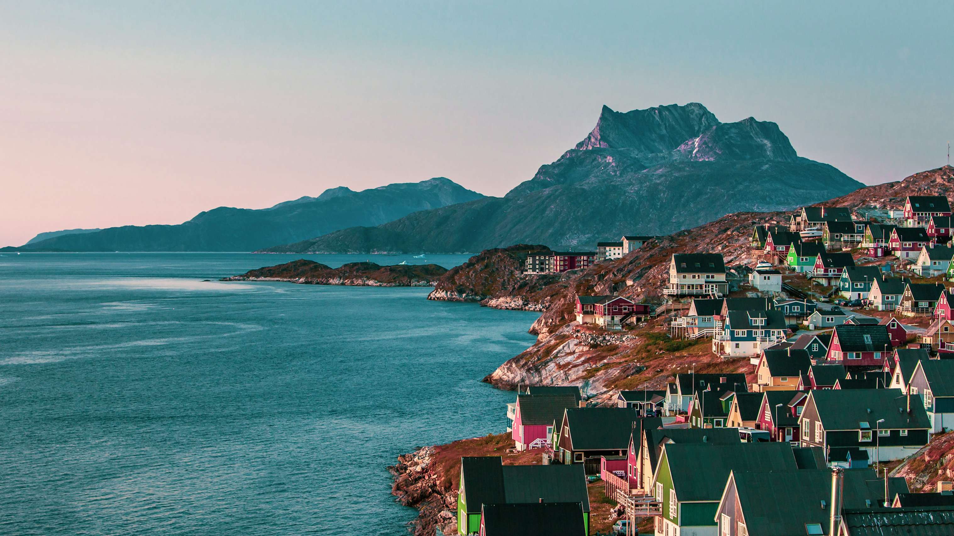 Twilight hues over a picturesque Greenlandic coastal village with colorful houses and a mountain backdrop.