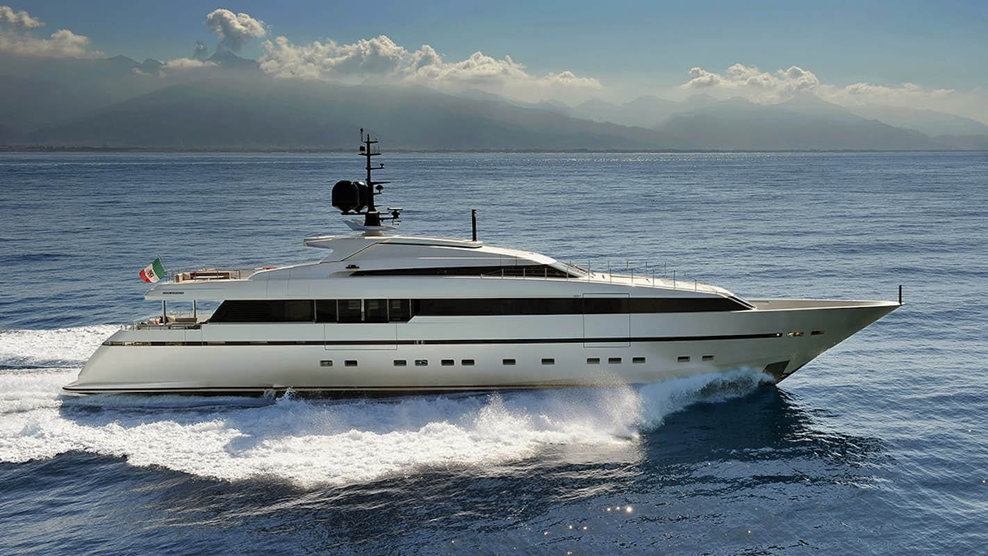 The Sanlorenzo 40 Alloy yacht, with the Italian flag, glides through blue waters with a mountain range in the background, available for sale through Northrop & Johnson.