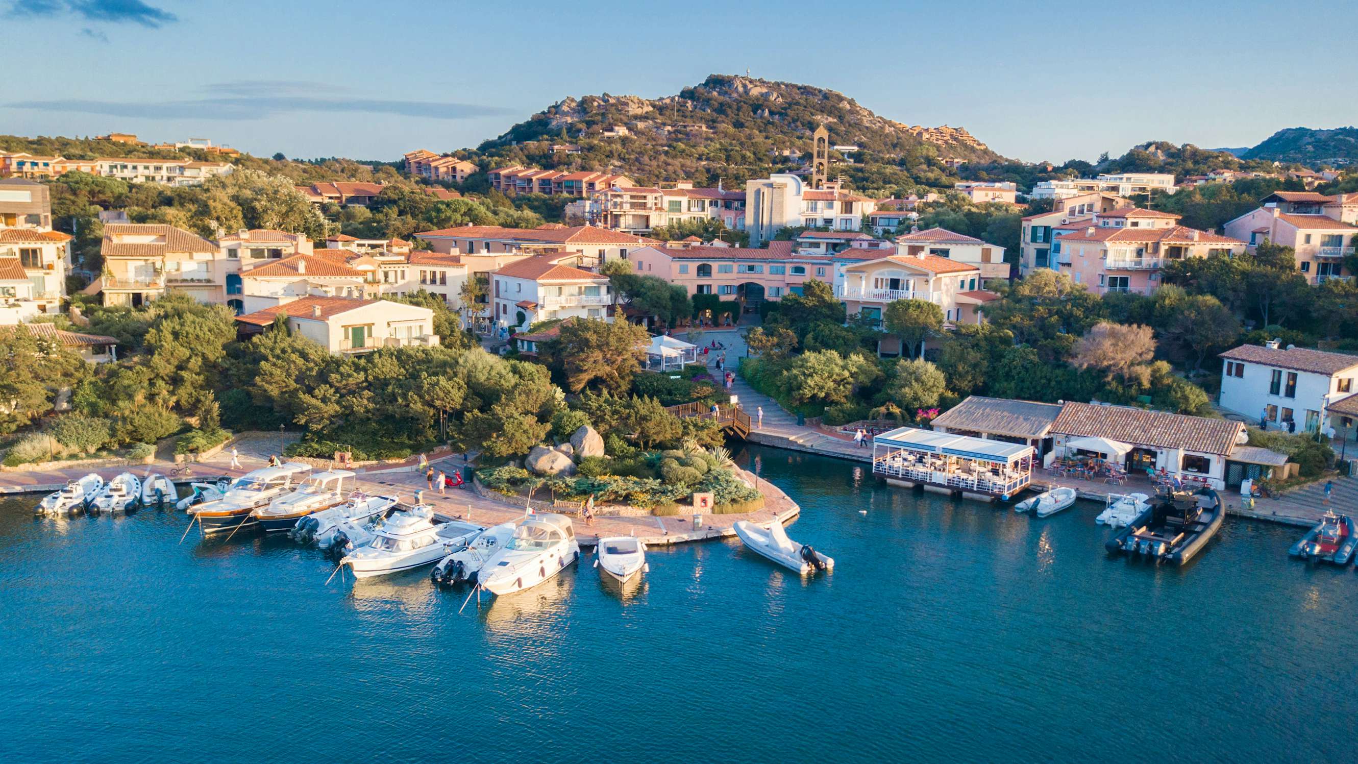 Aerial perspective of a Sardinian marina with yachts docked in crystal-clear waters.