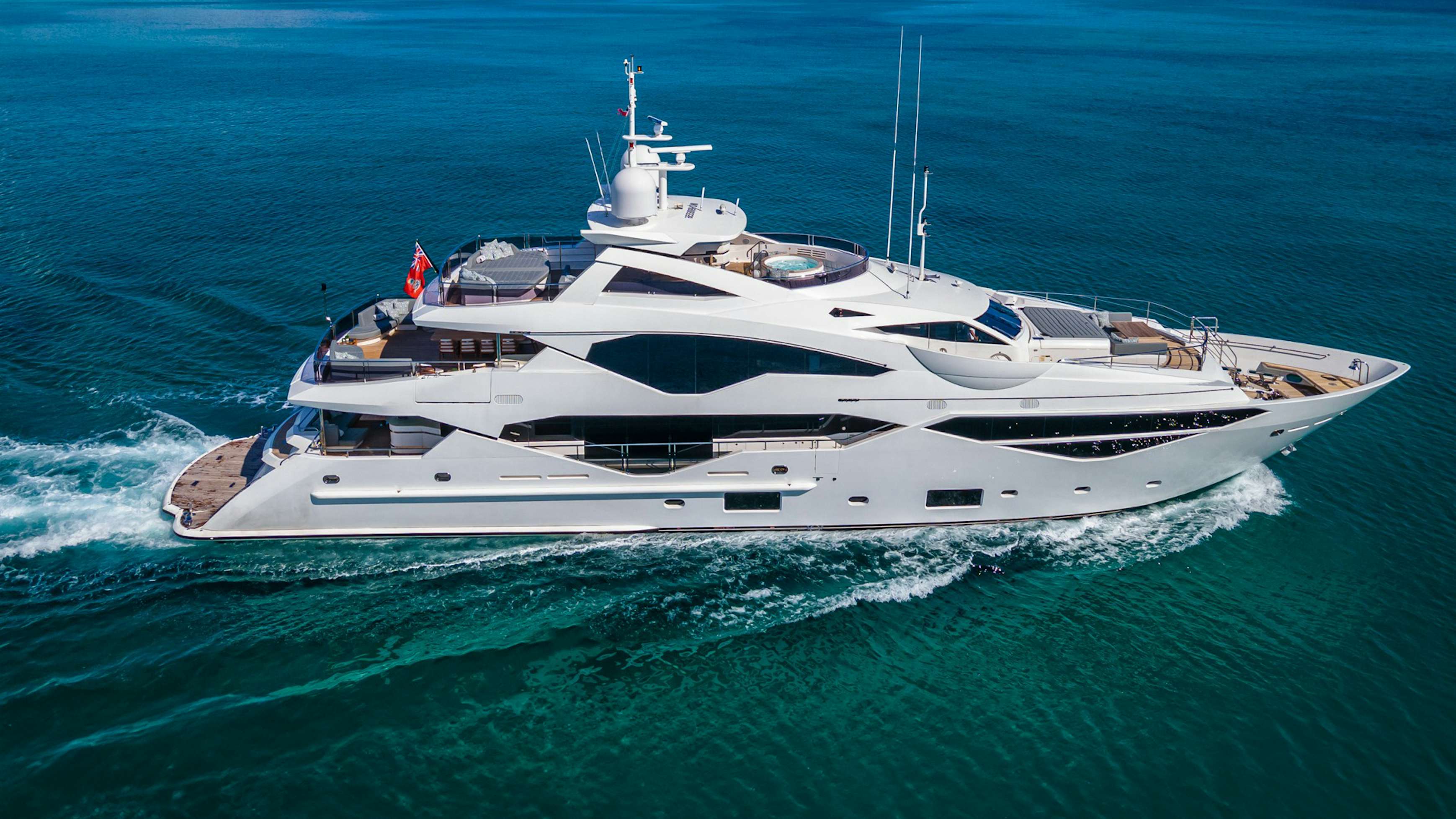 Aerial view of the Sunseeker 40 yacht sailing through turquoise waters, with a clear sky above and a hint of coastline in the distance.