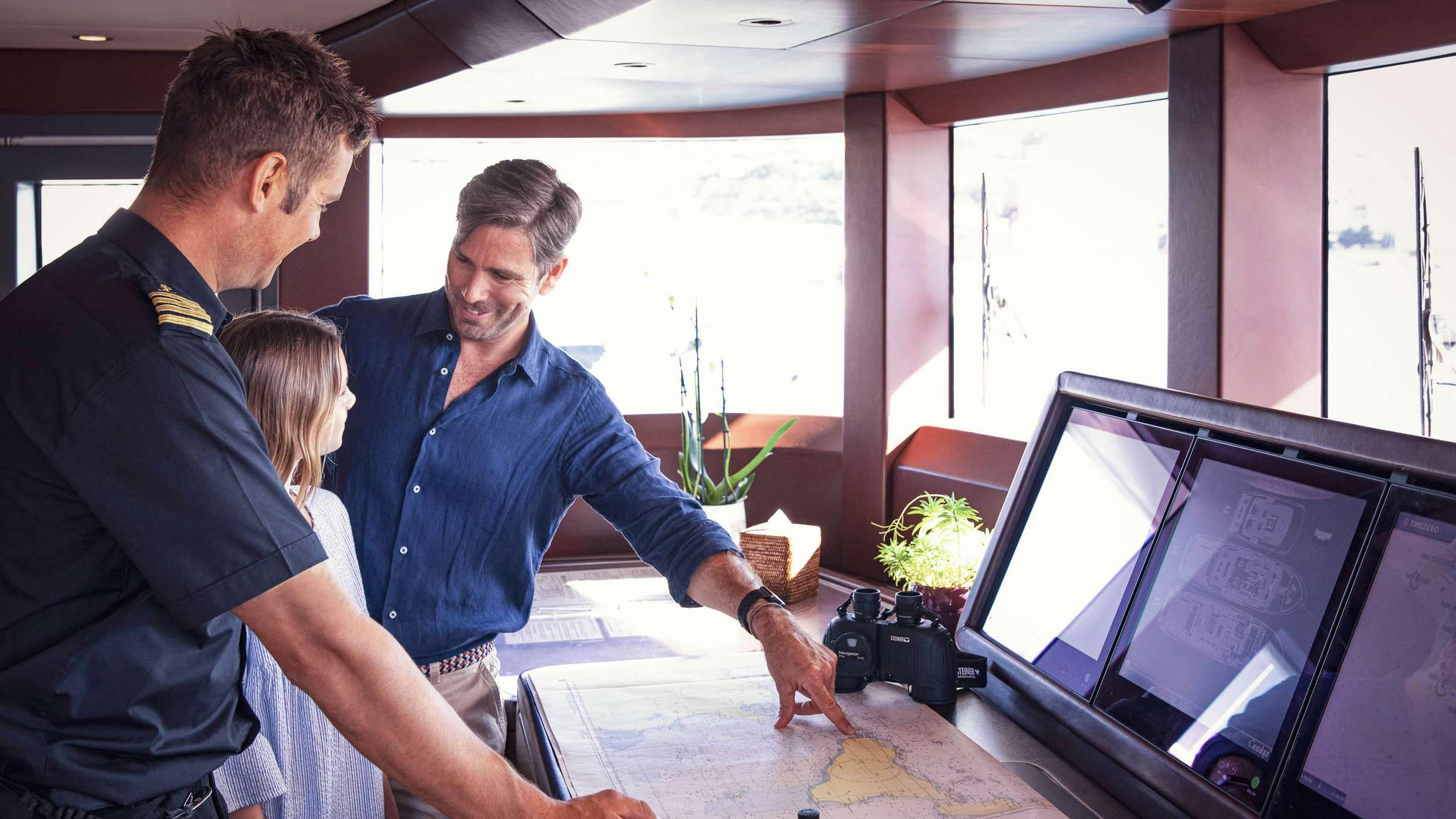 Father and daughter looking at a map with the captain on board a superyacht | Yacht Charter | Northrop & Johnson